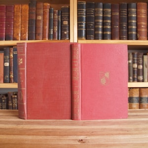 May include: A red hardcover book with gold lettering on the spine. The title is "The Works of Edgar Allan Poe" and the author is "Edited by Edmund Clarence Stedman and George Edward Woodberry".