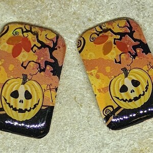 May include: A pair of Halloween-themed earrings with a jack-o'-lantern design. The earrings are made of glass and have a black, orange, and yellow color scheme.