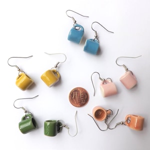 May include: A collection of miniature ceramic mug earrings in various colors, including blue, yellow, pink, green, and orange. Each earring features a small, detailed mug design with a silver-tone hook. A penny is included for size reference.