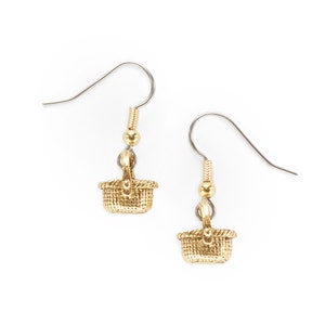 May include: A pair of gold-toned earrings featuring a small woven basket charm. The earrings have a simple hook closure.