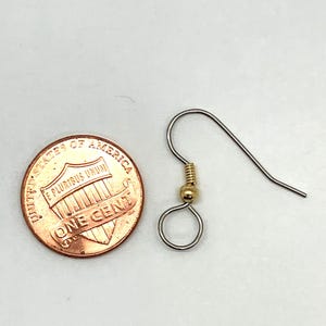 May include: A silver earring hook with a gold-toned bead. The earring hook is about the size of a US penny.