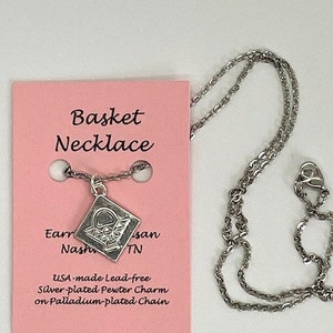 May include: A silver-plated pewter charm necklace with a basket design. The necklace is on a palladium-plated chain. The card reads "Basket Necklace", "Earr Nashi TN", "USA-made Lead-free Silver-plated Pewter Charm on Palladium-plated Chain".