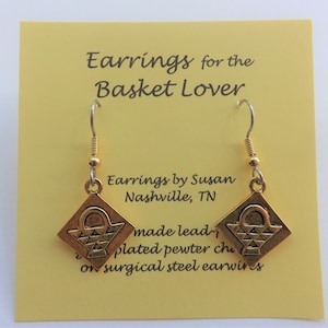 May include: Gold-tone earrings featuring a small basket design. The earrings are made of lead-free plated pewter and hang from surgical steel earwires. The card reads "Earrings for the Basket Lover" and "Earrings by Susan Nashville, TN".
