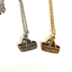 May include: Two necklaces with basket pendants. One necklace has a silver-colored chain and pendant, while the other has a gold-colored chain and pendant. The pendants are small, detailed basket shapes, perfect for a picnic-themed accessory.