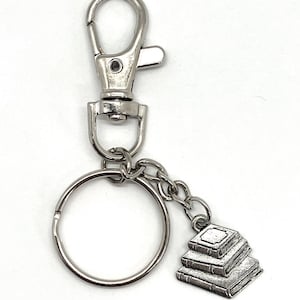 May include: Silver keychain with a stack of three books charm. The keychain has a silver split ring and a silver lobster clasp.