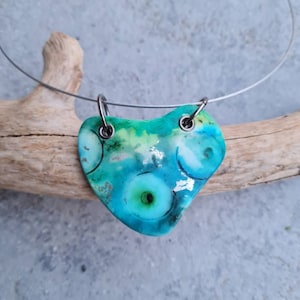 Könnte beinhalten: Eine Halskette mit einem türkisfarbenen Anhänger und einer silbernen Drahtkette. Der Anhänger ist herzförmig und hat ein wirbelndes Muster aus grünen und weißen Kreisen.