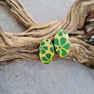 Può includere: Un paio di orecchini ovali con sfondo giallo e motivo floreale verde.