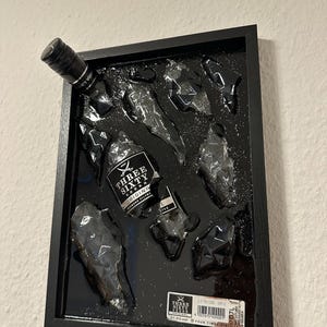 May include: A black rectangular frame containing a shattered Three Sixty Vodka bottle embedded in a glossy black resin surface. The glass shards are arranged to resemble the bottle shape, featuring the original label and a barcode sticker.
