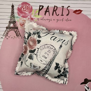 May include: A white fabric pillow with a floral design and the words "Paris is always a good idea" printed on it. The pillow has a scalloped edge and a vintage Parisian theme.