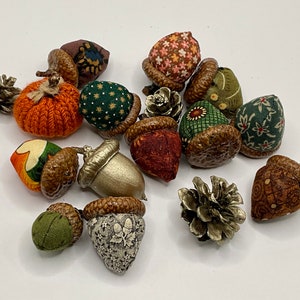 May include: A collection of 15 handmade fabric acorns in various patterns and colors, including green, brown, orange, and red. The acorns are made with a variety of fabrics, including floral prints, plaid, and solid colors. Some of the acorns have a brown felt cap, while others have a gold cap. The acorns are perfect for adding a touch of fall decor to your home.