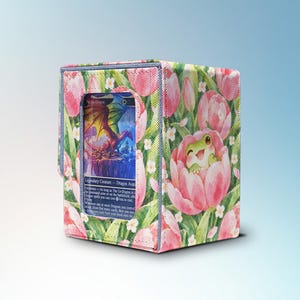 May include: A rectangular card storage box featuring a vibrant pattern of pink tulips and green leaves. A small, smiling green frog is illustrated peeking out from a tulip. A clear window on the front displays a trading card with a dragon illustration.