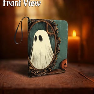 May include: A Halloween-themed wallet featuring a vintage-style illustration of a ghost in a decorative frame. The wallet has a black wrist strap and a pumpkin graphic. The words "Front View" are at the top.