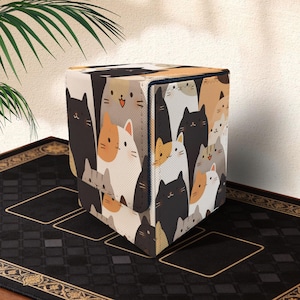 Puede incluir: Un cubo de almacenamiento con un patrón repetido de gatos de dibujos animados en negro, blanco, naranja y gris. Los gatos tienen caras simples y están muy juntos. El cubo tiene un borde azul oscuro.