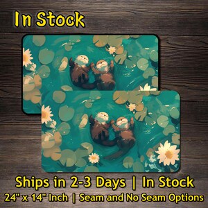 May include: Two rectangular mouse pads featuring an illustration of two otters floating in a pond with lily pads and flowers. The mouse pads are 24 inches by 14 inches. The text "In Stock" is at the top.