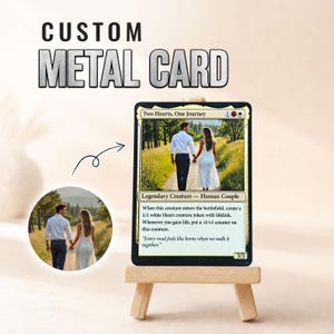 May include: A custom metal card displayed on a small wooden easel. The card features a photograph of a couple walking on a path, with the text Two Hearts, One Journey, Legendary Creature - Human Couple, and a quote at the bottom of the card.