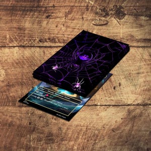 May include: A black card deck featuring a purple spiderweb design with a large spider and smaller spiders. The deck is partially covering a card with text that reads "Land - Swamp Mountain Forest". The background is a wooden surface.