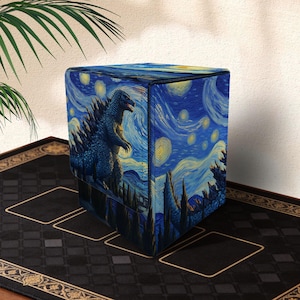 Puede incluir: Una caja de almacenamiento cúbica con una ilustración azul de Godzilla sobre un cielo estrellado, que recuerda el estilo de Van Gogh. La caja es principalmente azul con acentos amarillos y blancos.