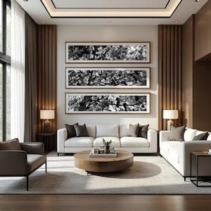 Puede incluir: Un salón moderno con tres impresiones enmarcadas en blanco y negro de la naturaleza sobre un sofá blanco. La habitación cuenta con una mesa de centro redonda de madera, un sillón gris y una alfombra de tonos neutros. Dos lámparas a juego están en las mesas auxiliares.