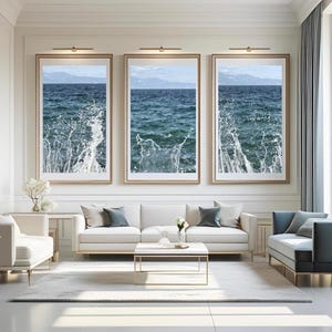 Puede incluir: Tres impresiones artísticas enmarcadas que representan olas del océano rompiendo. Las impresiones presentan tonos azules y blancos, con un marco dorado. La obra de arte se exhibe sobre un sofá y sillas blancos en una sala de estar moderna y luminosa.