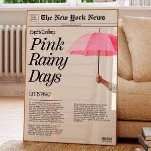 May include: A framed print designed to look like a newspaper front page. The headline reads "Pink Rainy Days" with an illustration of a pink umbrella. The text includes "The New York News" and additional articles.