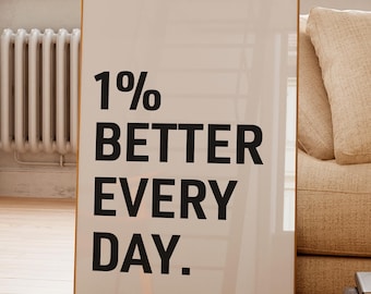 May include: A framed print with the text "1% BETTER EVERY DAY" in black against a cream background. The frame is gold. The print is leaning against a beige sofa in a well-lit room.