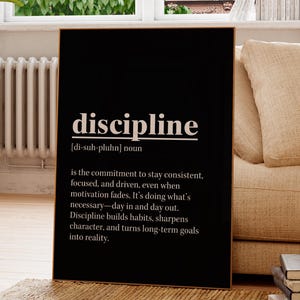 May include: A black framed print with the word 'discipline' in white, along with its definition. The definition reads: 'is the commitment to stay consistent, focused, and driven, even when motivation fades. It's doing what's necessary-day in and day out. Discipline builds habits, sharpens character, and turns long-term goals into reality.'