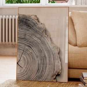 May include: A framed print displaying a detailed cross-section of a tree trunk, with concentric growth rings in grey and brown tones. The artwork is set in a room with neutral colours, near a window and a beige sofa, creating a natural aesthetic.