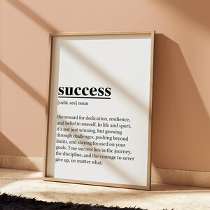May include: A framed print with the word "success" in a bold, black font at the top. The definition of success is written below in a smaller, black font. The frame is a light wood color, and the background is white.