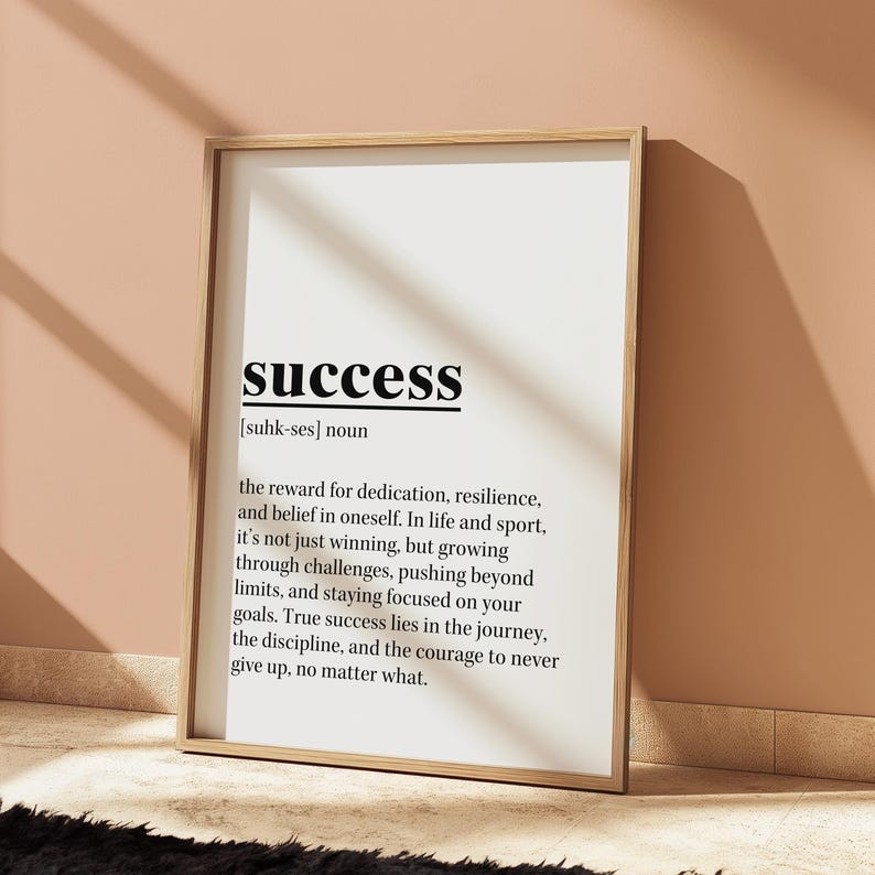 May include: A framed print with the word "success" in a bold, black font at the top. The definition of success is written below in a smaller, black font. The frame is a light wood color, and the background is white.