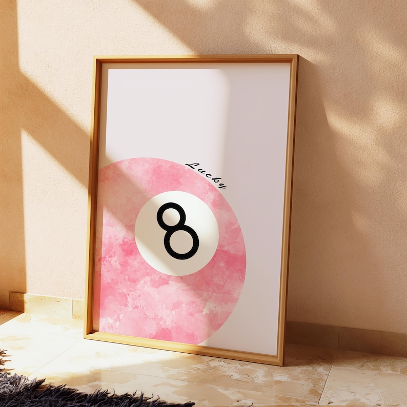 以下が含まれることがあります： ピンクの水彩画プリント。8の数字が黒で書かれたビリヤードボール。ボールの上に「Lucky」という文字が黒の筆記体で書かれている。
