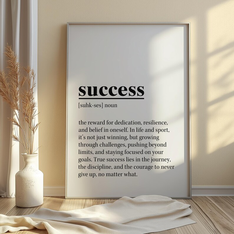 May include: A framed print with the word "success" in bold black letters at the top. Below, the definition of success is printed in black text. The print is displayed on a wooden floor, with a vase and decorative plant to the left.