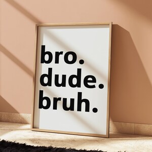 Puede incluir: Impresi&oacute;n enmarcada con las palabras "bro. dude. bruh." en negrita negra sobre un fondo blanco. El marco es de color madera clara, y la impresi&oacute;n est&aacute; apoyada contra una pared color melocot&oacute;n.