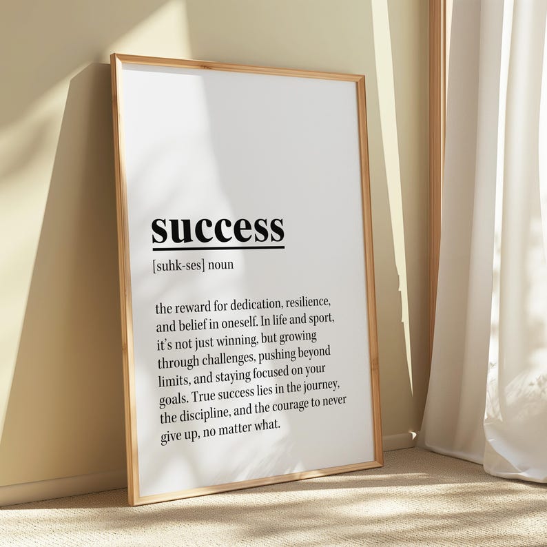May include: A framed print with the word "success" in bold black font. The definition of success is written below the word. The frame is a light brown color, and the background is a neutral beige.