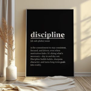 May include: A black framed print with the definition of "discipline" in white text. The definition includes the pronunciation, and a description of discipline's meaning. The print is displayed on a wooden floor.