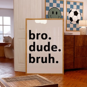 Puede incluir: Un cartel enmarcado con las palabras "bro. dude. bruh." en negrita negra. Se ven dos carteles enmarcados adicionales, uno con una carita sonriente y otro con un bal&oacute;n de f&uacute;tbol, ambos sobre un fondo a cuadros azul y blanco.