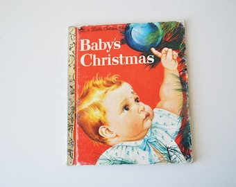 May include: Vintage children's book titled "Baby's Christmas." The cover features a baby reaching for a blue ornament on a Christmas tree, set against a red background. The book has a gold spine.