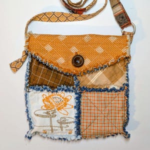 May include: A patchwork crossbody bag with a variety of fabrics in shades of orange, brown, and cream. The bag features a button closure and a long strap with patterned details. The design includes a floral embroidered square.