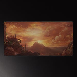 Może przedstawiać: Prostokątna podkładka pod mysz z fantastycznym krajobrazem o zachodzie słońca. Grafika przedstawia pasmo górskie, budynki i dramatyczne niebo w odcieniach pomarańczu, czerwieni i brązu. Podkładka ma czarną obwódkę.