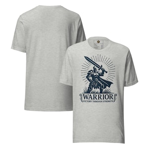 Könnte beinhalten: Hellgraues T-Shirt mit einer marineblauen Grafik eines Kriegers, der ein Schwert hält, mit dem Wort "WARRIOR" und dem Text "VICTORY THROUGH STRENGTH". Die Rückseite des T-Shirts ist schlicht hellgrau.