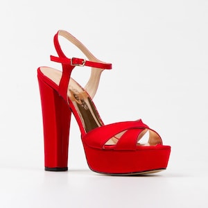 Puede incluir: Sandalias de plataforma de satén rojo con tacón grueso y correa de tobillo.