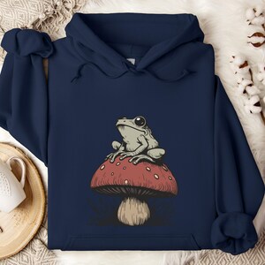 May include: A navy blue hoodie with a graphic of a green frog sitting on a red and white mushroom.