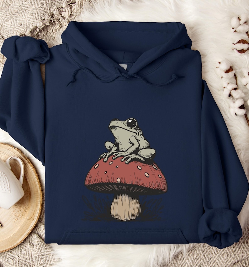 May include: A navy blue hoodie with a graphic of a green frog sitting on a red and white mushroom.