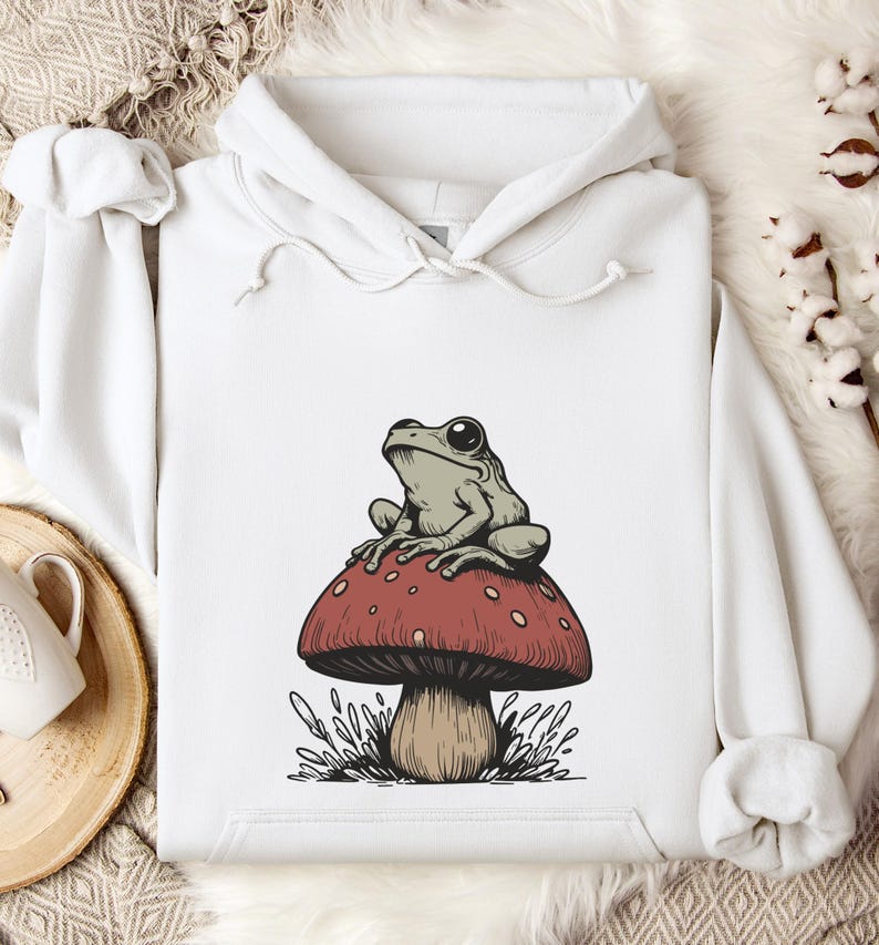 May include: White hoodie with a graphic of a green frog sitting on a red and white mushroom.