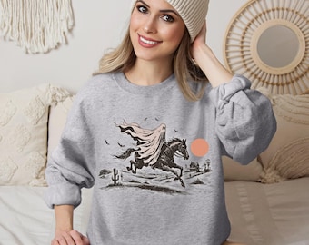 May include: A gray sweatshirt featuring a black and white illustration of a cloaked figure riding a horse through a desert landscape. The design includes a peach-colored sun and black bats. The sweatshirt is a crew neck style.