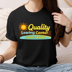 May include: Black t-shirt with a graphic design featuring a yellow sun, the word "Quality" in yellow, and the text "Learing Center" and "1-800-FRAUD". The design is printed on the front of the shirt.