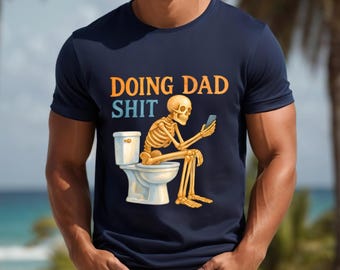 May include: Navy blue t-shirt with the text "DOING DAD SHIT" in orange and blue. The graphic shows a skeleton sitting on a toilet, looking at a phone. The skeleton is yellow and the toilet is white.