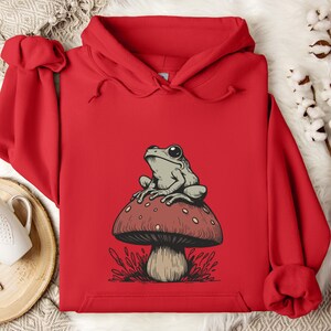 May include: Red hooded sweatshirt with a graphic of a green frog sitting on a red and white mushroom.
