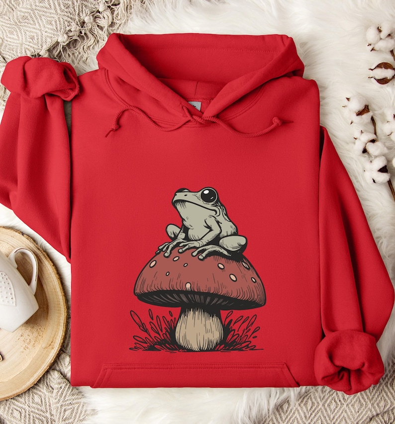May include: Red hooded sweatshirt with a graphic of a green frog sitting on a red and white mushroom.