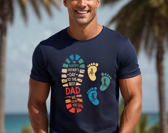 May include: Navy blue t-shirt with a colorful graphic. The graphic includes a footprint design with the text "Happy Father's Day to the Best Dad We Love You." There are also three colorful footprints with names.