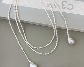 May include: A long, layered pearl necklace with two large, irregular pearls at the ends. The necklace is white and the pearls are a creamy white.